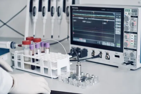 gloved hands in a lab in front of vials and measuring tool